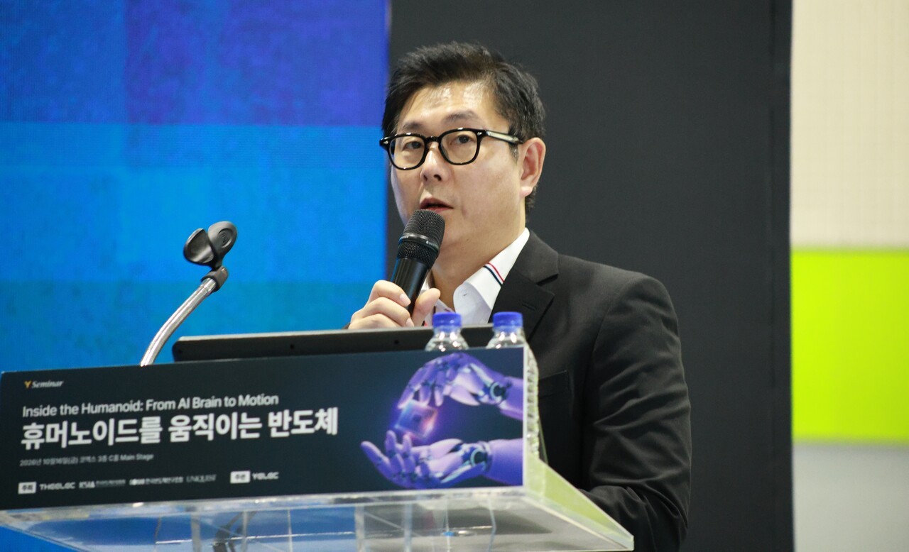 A speaker gives a presentation at the Inside the Humanoid: From AI Brain to Motion seminar, standing at a podium with a microphone and a computer setup.