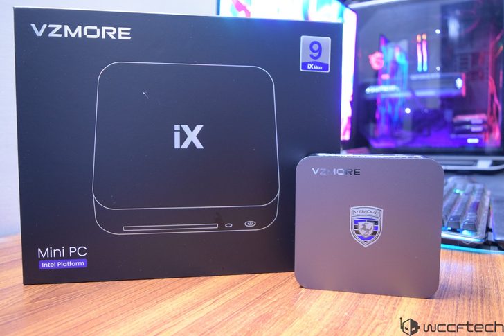 A VZMORE iX Mini PC and its packaging with 'Intel Platform' text displayed on a wooden surface in front of a gaming setup.