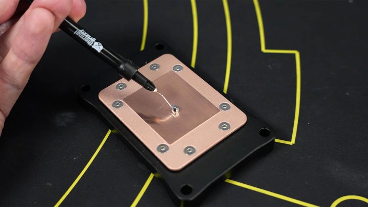 A hand applies thermal paste using a Thermal Grizzly syringe onto a copper CPU plate.