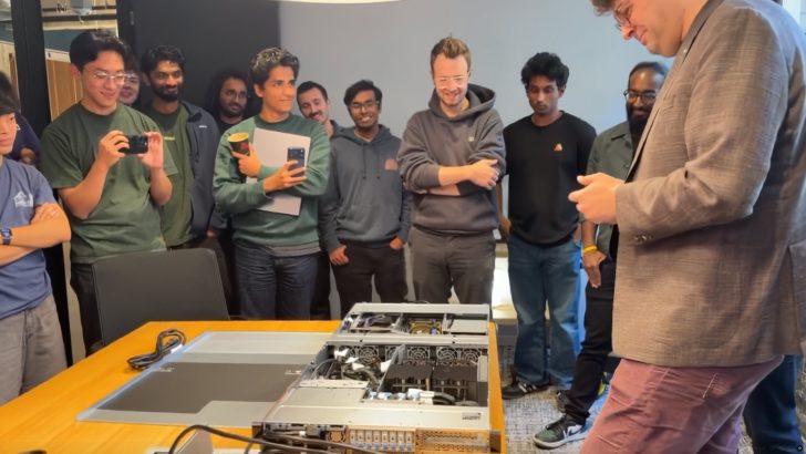 A group of people gathers around a table looking at an open AI server with NVIDIA A100 GPUs inside.